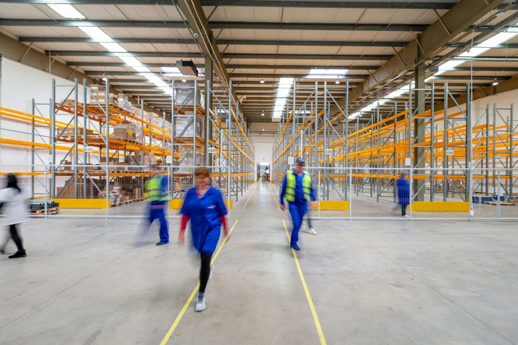 Workers crossing a busy warehouse floor between tall racking