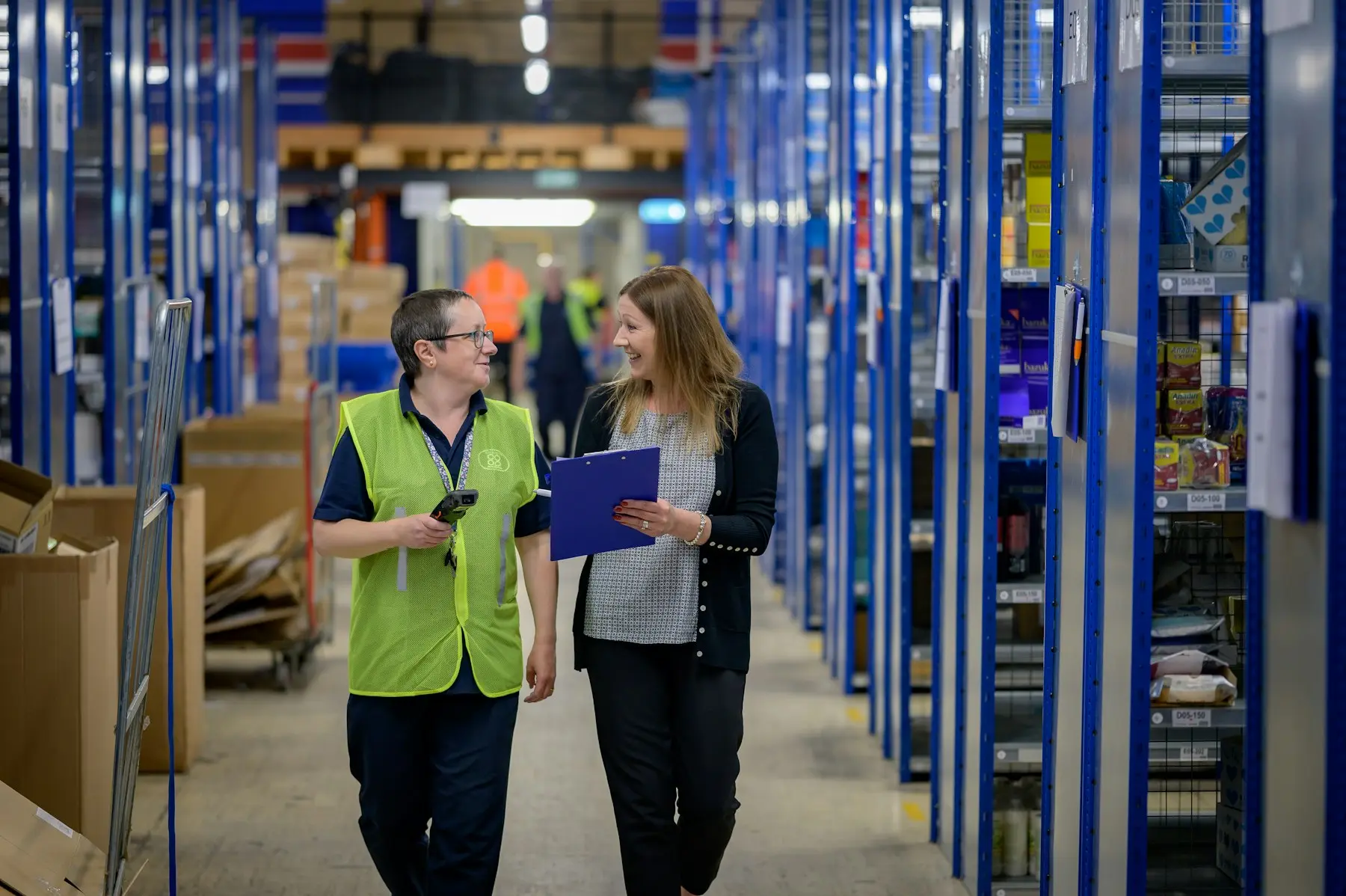 Two people walking a warehouse aisle between tall blue shelving